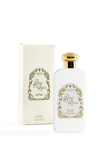 White bottle with gold accents and decorative label next to a matching box on a white background