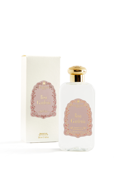 Bottle of rosa gardenia bath and shower gel with its packaging next to it on a blank white studio background. Packaging features a floral trim around the logo.